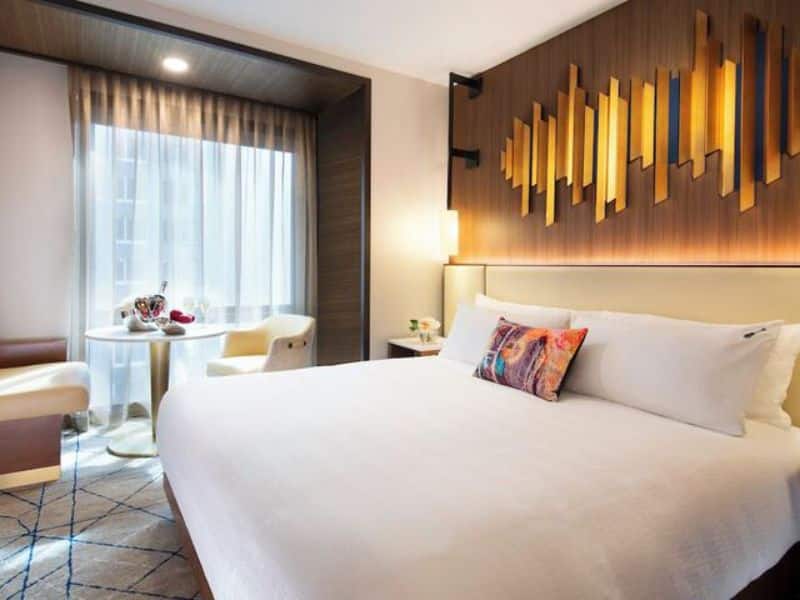 Stylish hotel room at Hard Rock Hotel New York featuring a king-size bed, modern decor, and a cozy seating area with a table, showcasing luxury accommodations in the Theater District.