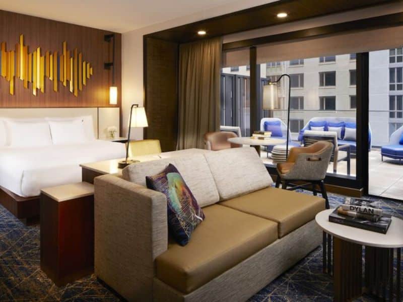 Stylish hotel room at Hard Rock Hotel New York featuring a king-sized bed, seating area, modern decor, and large windows with outdoor terrace access.