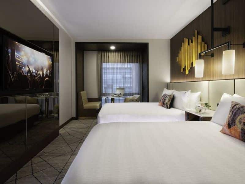 Stylish hotel room at Hard Rock Hotel New York featuring two beds, modern decor, a large TV, and a seating area with a view.
