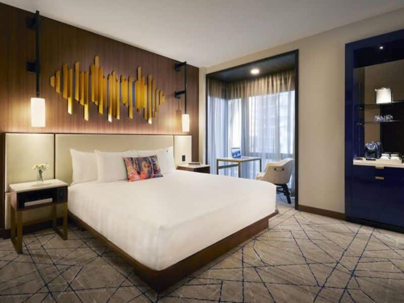 Stylish hotel room at Hard Rock Hotel New York featuring a queen bed, modern decor, and natural light from large windows.