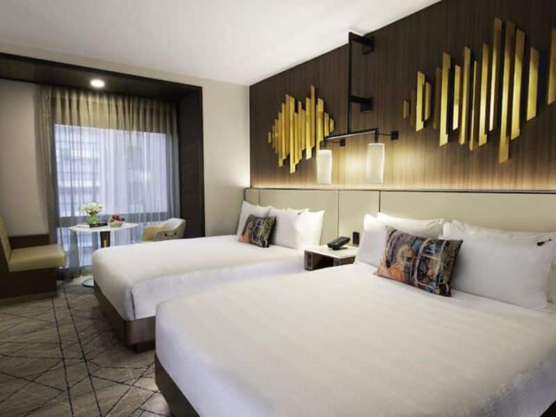 Stylish hotel room at Hard Rock Hotel New York featuring two beds, modern decor, and a seating area with a table, emphasizing luxurious accommodations and comfort.