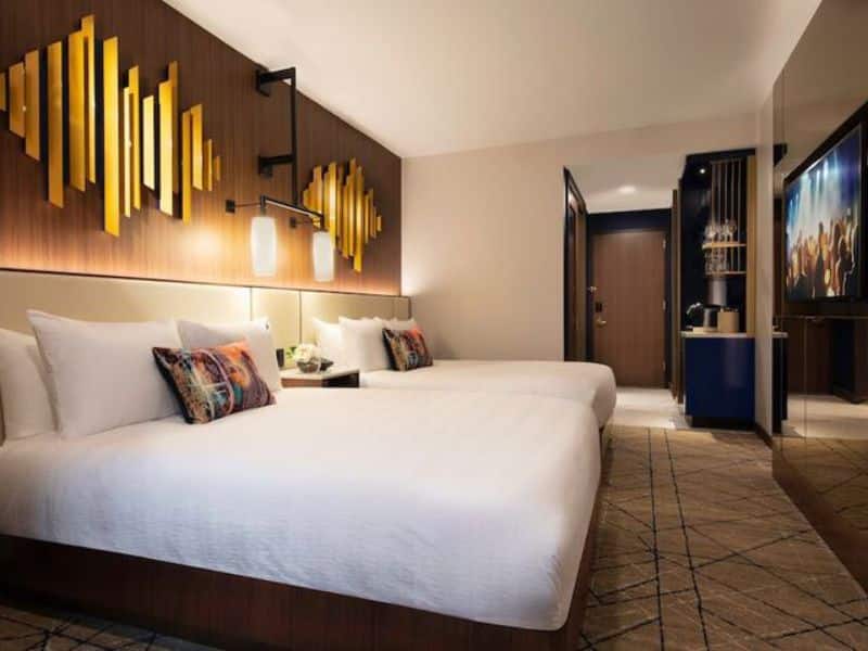 Stylish hotel room at Hard Rock Hotel New York featuring two beds, modern decor, artistic wall accents, and amenities like a coffee maker and TV.