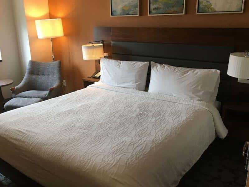Cozy hotel room at Hilton Garden Inn Long Island City featuring a king-size bed, armchair, bedside lamps, and artwork, emphasizing comfort and modern design.
