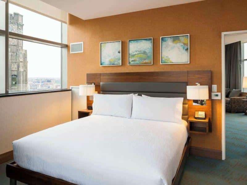 Cozy hotel room at Hilton Garden Inn Long Island City with a queen bed, modern decor, and large windows showcasing city views.
