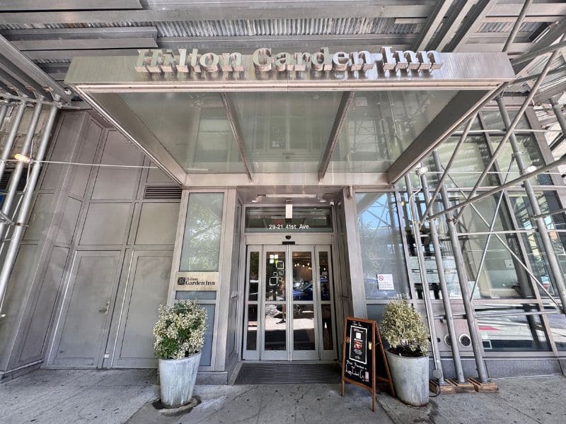Hilton Garden Inn Long Island City entrance with modern architecture, welcoming sign, and signage for nearby amenities.
