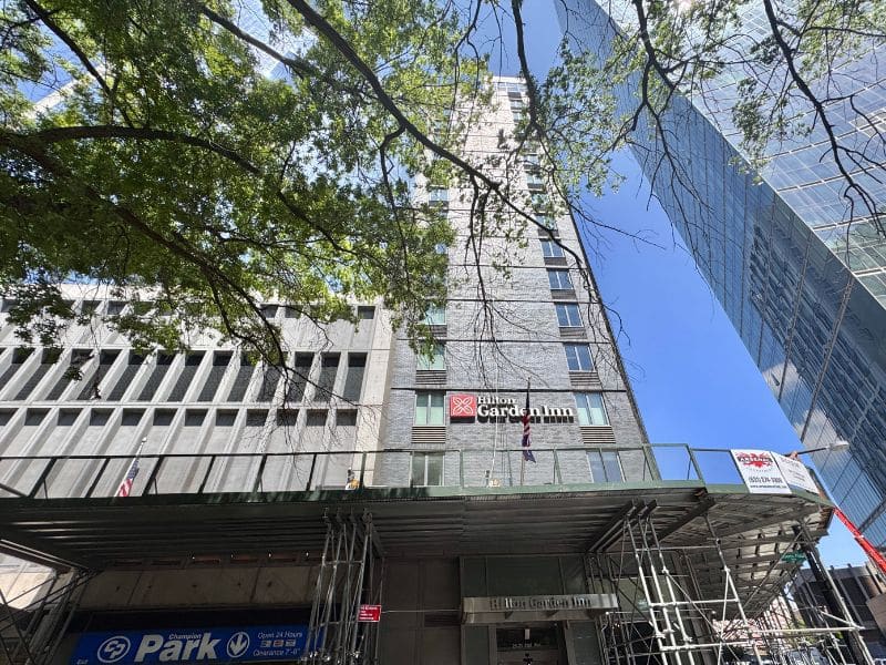Hilton Garden Inn Long Island City exterior view with scaffolding, showcasing hotel branding and surrounding urban landscape.