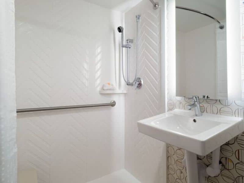 Modern hotel bathroom featuring a shower with grab bars, a sleek sink, and stylish herringbone tile design, emphasizing accessibility and comfort at Holiday Inn New York City – Wall Street.