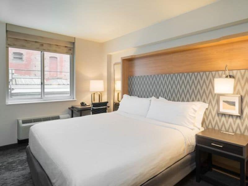 Modern hotel room at Holiday Inn New York City – Wall Street, featuring a large bed, desk, and window with natural light.