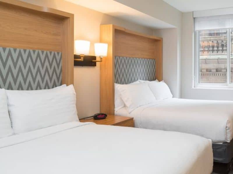 Modern hotel room with two beds, stylish headboards, bedside lamps, and a window, showcasing a comfortable stay at Holiday Inn New York City – Wall Street by IHG.