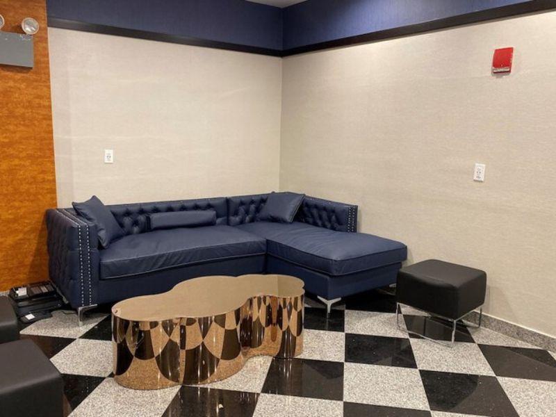 Cozy lobby lounge area with navy blue sectional sofa, decorative gold coffee table, and modern black ottoman, reflecting the inviting atmosphere of Hotel Key in Flushing, NY.