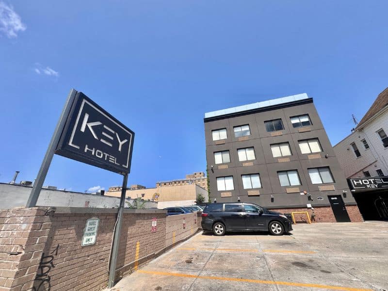 Hotel Key exterior view with prominent signage, showcasing modern architecture and parking area in Flushing, New York, emphasizing accessibility and urban setting.