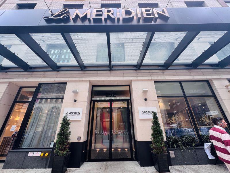 Le Meridien New York Fifth Avenue entrance featuring modern architecture, glass awning, and welcoming entrance, surrounded by cityscape elements.