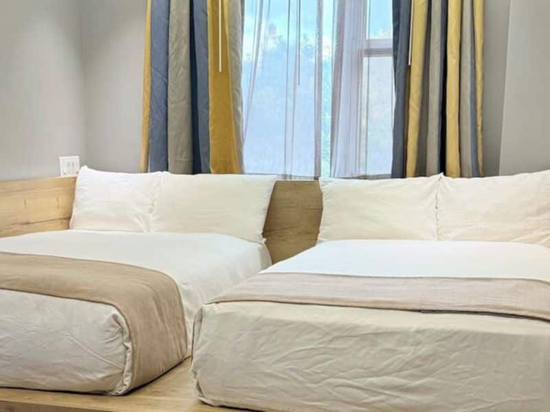 Comfortable hotel room at Madison LES Hotel featuring two beds, large window with natural light, and modern decor with colorful curtains.