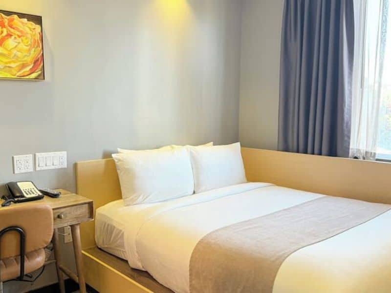 Cozy hotel room at Madison LES Hotel featuring a queen bed, desk, and modern decor, emphasizing comfort and convenience for travelers.