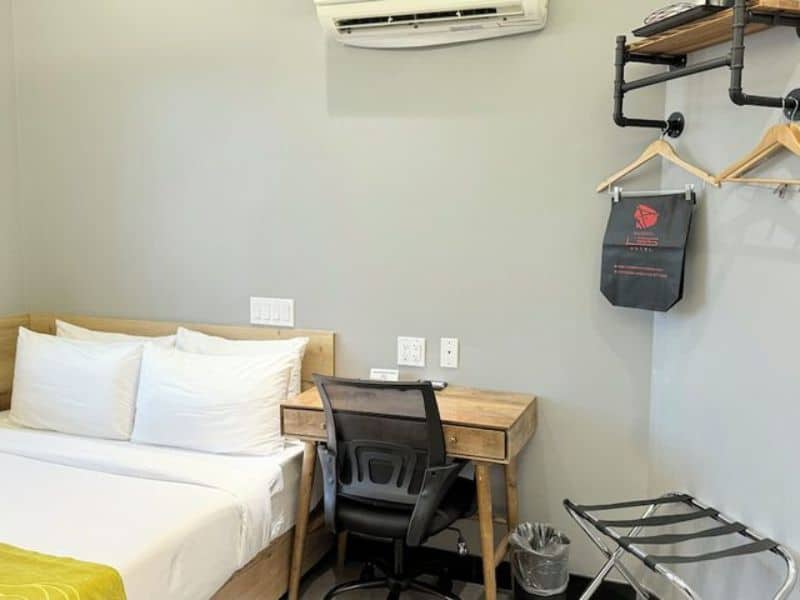 Cozy hotel room at Madison LES Hotel featuring a bed with white linens, wooden desk and chair, air conditioning unit, and modern decor, ideal for business travelers and tourists.