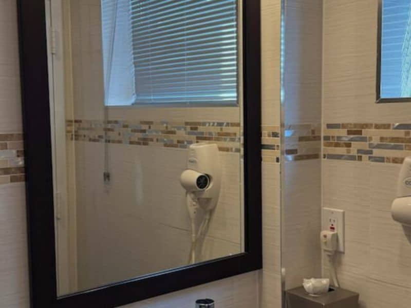 Bathroom mirror with hairdryer and modern tile accents, reflecting natural light, showcasing amenities at Madison LES Hotel.