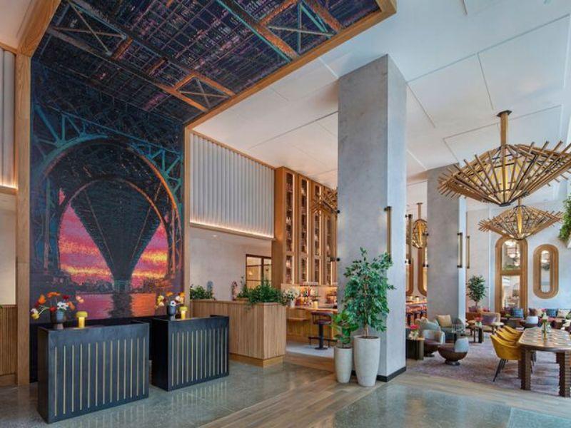 Stylish hotel lobby at Moxy Brooklyn Williamsburg featuring vibrant mural, modern decor, and seating areas, highlighting the inviting atmosphere for guests.