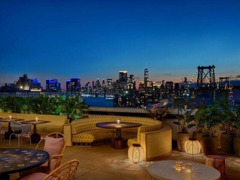 Rooftop bar at Moxy Brooklyn Williamsburg with cozy seating, city skyline view, and evening ambiance.