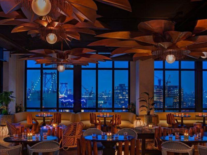 Rooftop bar at Moxy Brooklyn Williamsburg featuring stylish decor, ambient lighting, and views of the city skyline at dusk.