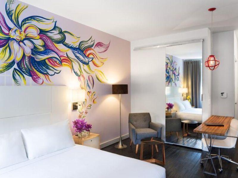 Stylish hotel room at NU Hotel Brooklyn featuring vibrant mural, modern decor, comfortable bed, seating area, and ambient lighting.