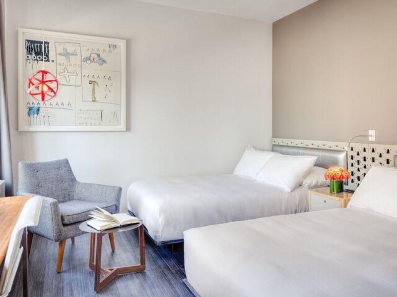 Stylish hotel room at NU Hotel Brooklyn featuring two beds, modern decor, a cozy seating area, and artistic wall art, highlighting the boutique experience and amenities.