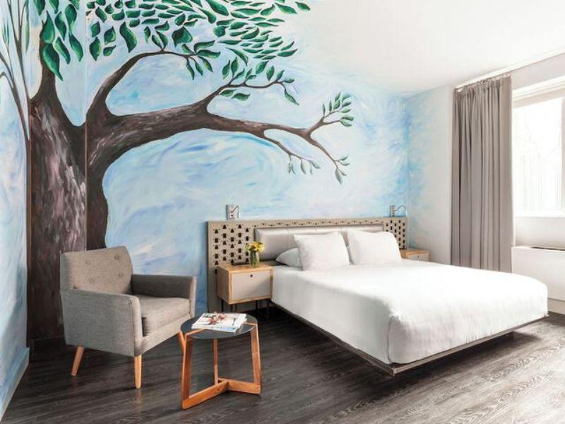 Stylish hotel room at NU Hotel Brooklyn featuring a mural of a tree, modern furnishings, a cozy bed, and a comfortable seating area.