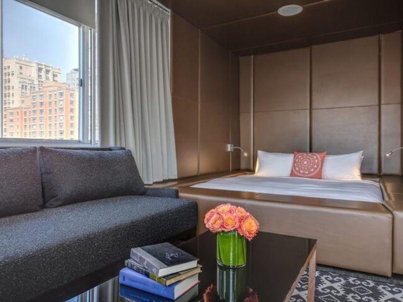 Stylish loft-style room at NU Hotel Brooklyn featuring a cozy bed, modern furnishings, and a sofa, with a view of the city skyline.