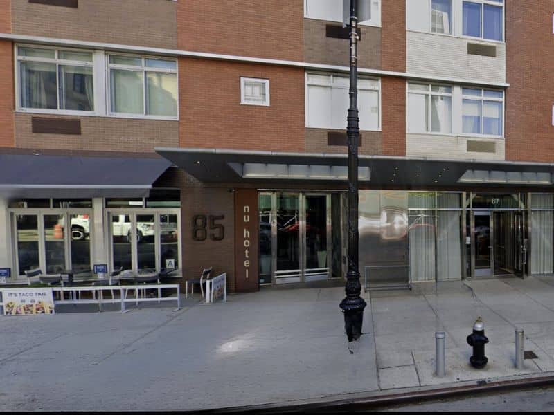 NU Hotel Brooklyn entrance with modern architecture, featuring the number 85, large glass doors, and outdoor seating area.