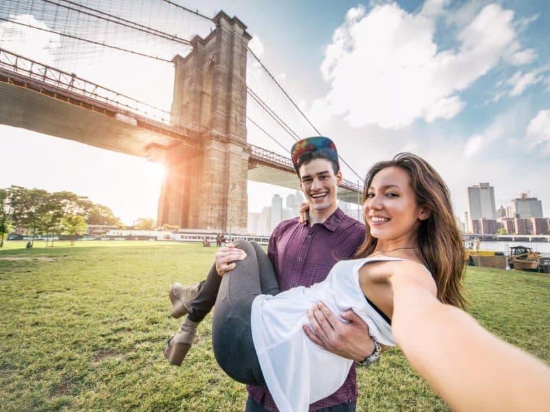 Couple posing joyfully in front of Brooklyn Bridge during a private car tour exploring The Godfather filming locations in NYC.