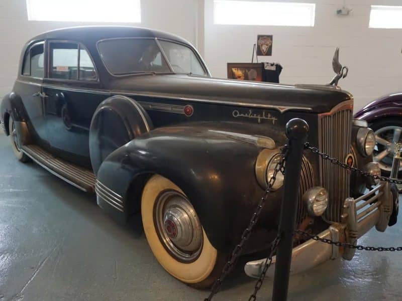 Classic black car, reminiscent of The Godfather era, displayed in a museum setting, featuring vintage design elements and whitewall tires, symbolizing iconic cinematic history.