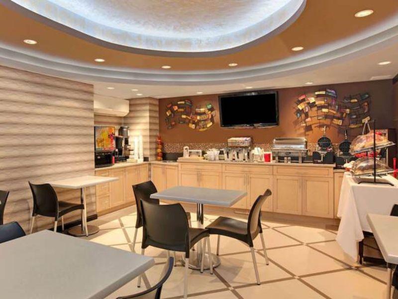 Breakfast area at Ramada by Wyndham Bronx featuring tables, chairs, buffet setup with food and beverage stations, modern decor, and a flat-screen TV.