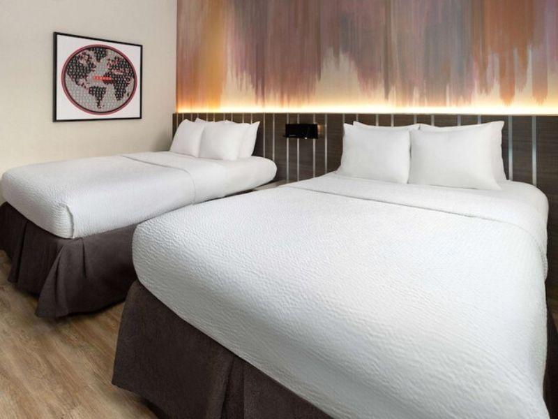 Cozy hotel room at Ramada by Wyndham Bronx featuring two beds, modern decor, and a colorful wall art backdrop, highlighting comfortable accommodations for travelers.