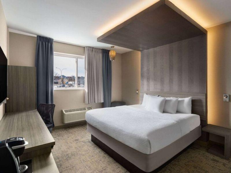 Cozy hotel room at Ramada by Wyndham Bronx featuring a queen bed, flat-screen TV, desk, and window with natural light.