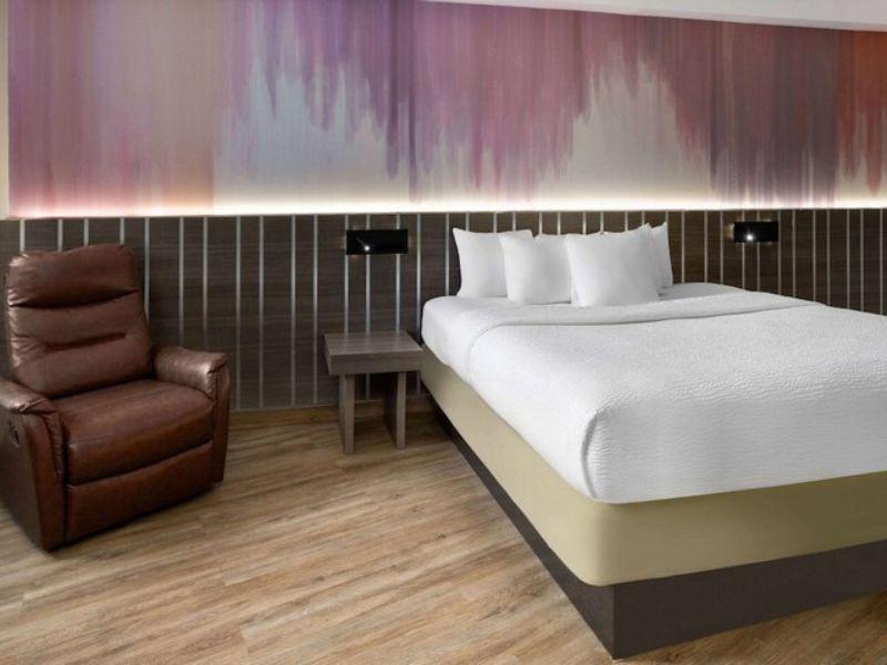 Cozy hotel room at Ramada by Wyndham Bronx featuring a comfortable bed, reclining chair, and modern decor with warm lighting.