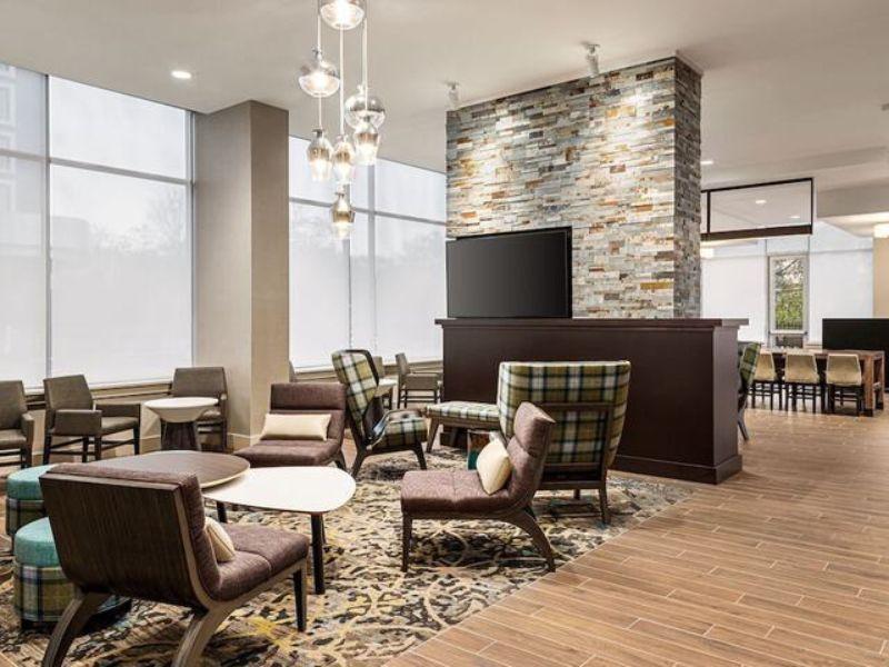 Welcoming lobby lounge of Residence Inn by Marriott New York JFK Airport, featuring modern seating, a stone accent wall, and a cozy atmosphere, ideal for travelers seeking comfort and convenience near JFK Airport.