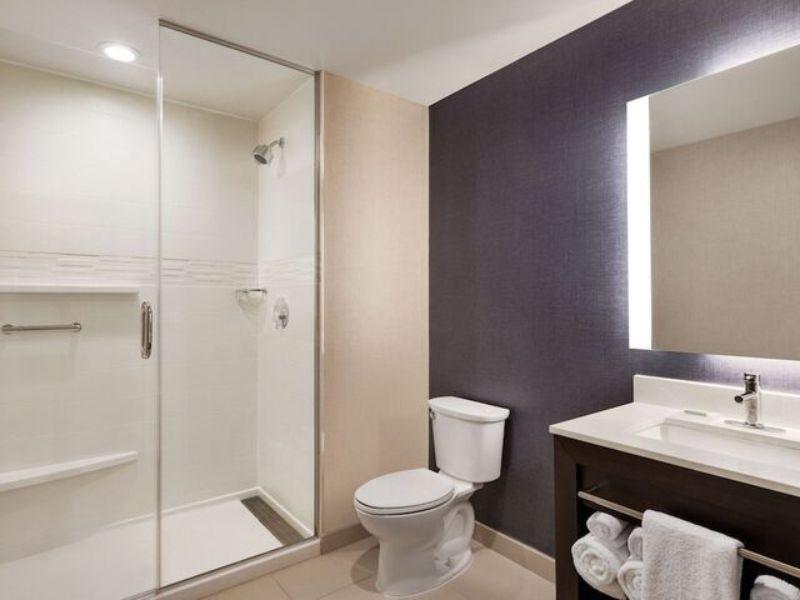 Modern hotel bathroom with glass shower, toilet, and vanity, featuring contemporary design elements and neutral color scheme, reflecting amenities at Residence Inn by Marriott New York JFK Airport.