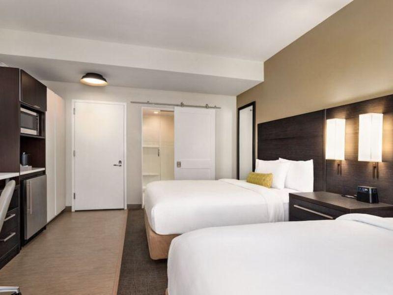 Modern hotel room at Residence Inn by Marriott New York JFK Airport featuring two beds, kitchenette, and contemporary decor, ideal for travelers seeking comfort and convenience near JFK Airport.