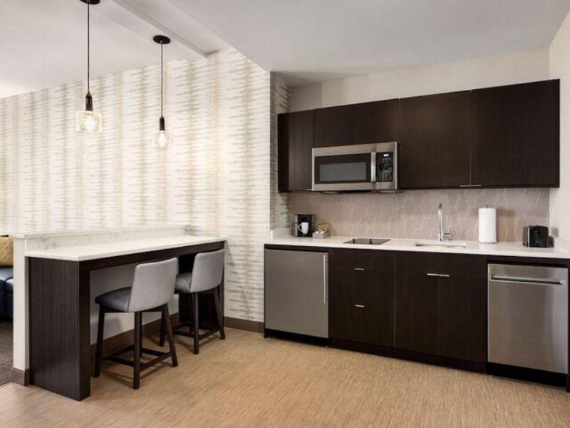 Modern kitchenette in Residence Inn by Marriott New York JFK Airport, featuring stainless steel appliances, bar seating, and stylish decor, highlighting amenities for travelers.
