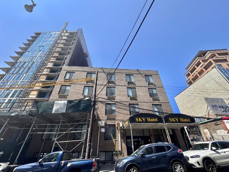 Sky Hotel exterior view with modern architecture, scaffolding, and vehicles, located in Flushing near LaGuardia Airport, showcasing budget-friendly accommodations.