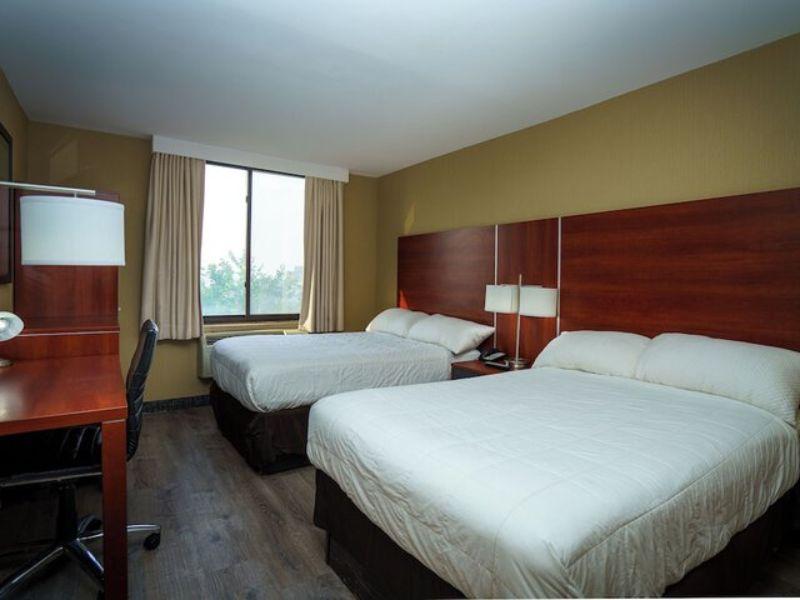 Hotel room at Sky Hotel Flushing featuring two beds, a desk, and a window with natural light, highlighting comfort and convenience near LaGuardia Airport.