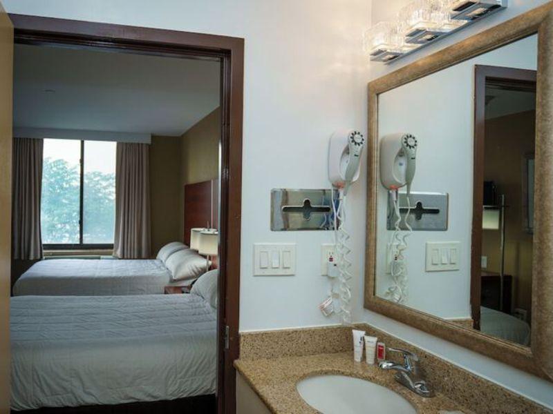 Hotel bathroom view with sink and mirror, showcasing two beds in the background, emphasizing amenities for guests near LaGuardia Airport.