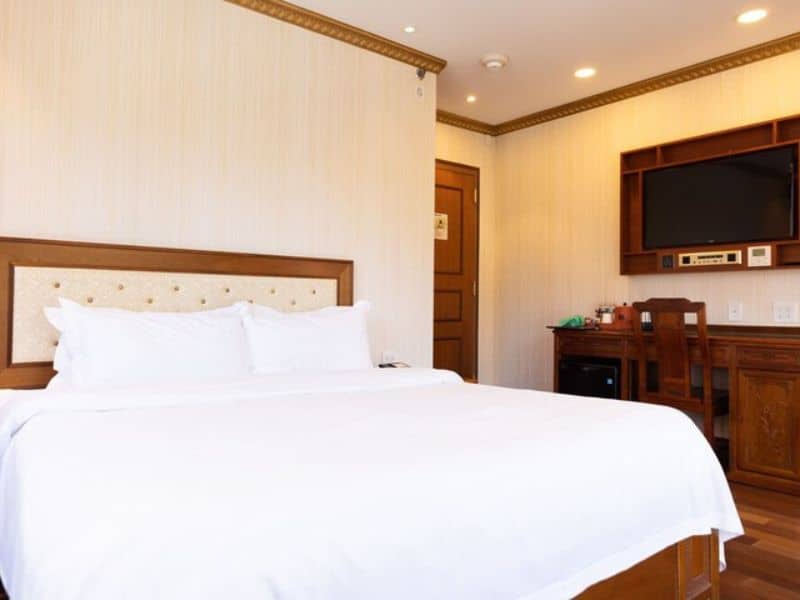 Elegant hotel room at The Allen Hotel featuring a king-size bed, wooden furnishings, desk area, and wall-mounted flat-screen TV, showcasing modern comforts and inviting ambiance in the Lower East Side of NYC.