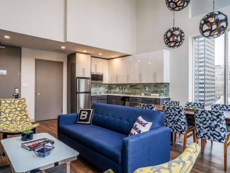 Stylish hotel suite at The Bernic Hotel New York City, featuring modern furnishings, a blue sofa, and a dining area with large windows showcasing city views.