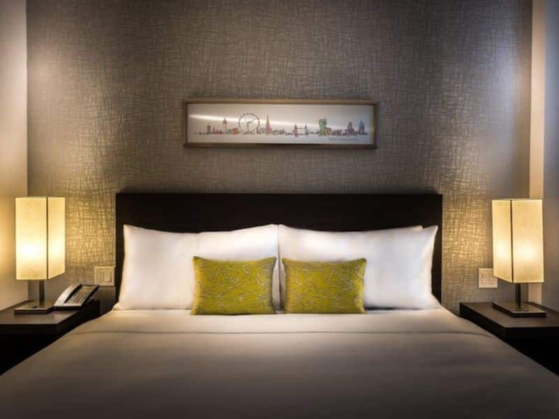 Stylish hotel room at The Bernic Hotel New York City, featuring a king-sized bed with decorative green pillows, bedside lamps, and a cityscape artwork above the headboard, emphasizing modern comfort and design.
