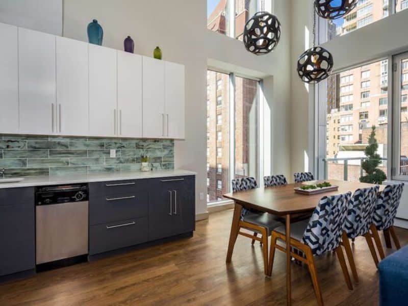 Stylish kitchen and dining area at The Bernic Hotel New York City, featuring modern cabinetry, a large dining table, and ample natural light from floor-to-ceiling windows.
