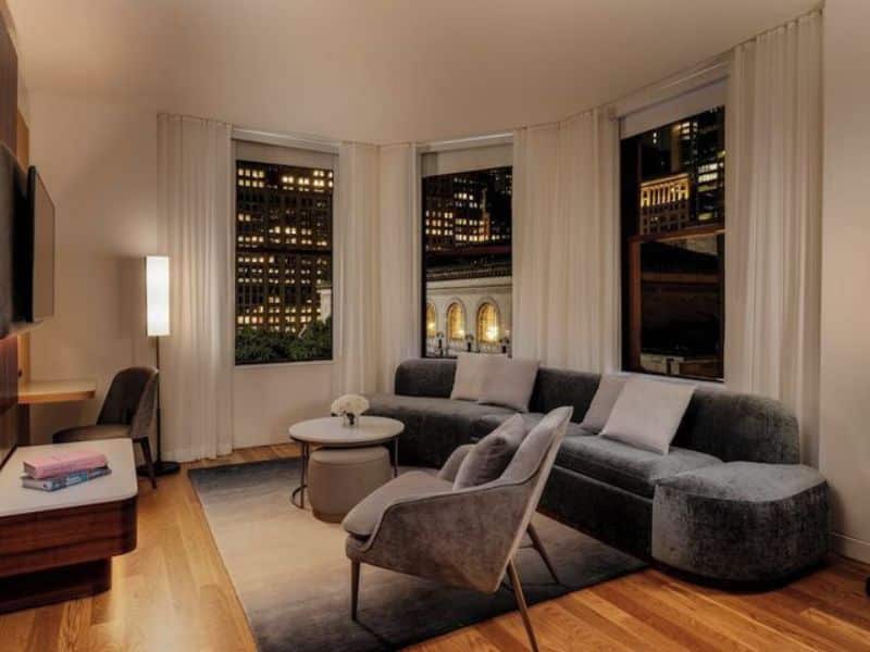 Stylish hotel room at The Bryant Park Hotel featuring a modern seating area, large windows with city views, and elegant decor.