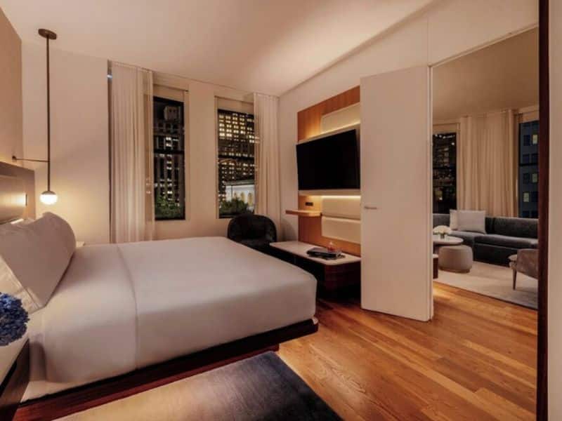 Stylish hotel room at The Bryant Park Hotel featuring a queen bed, hardwood floors, flat-screen TV, and large windows with city views.