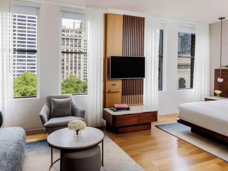 Stylish hotel room at The Bryant Park Hotel featuring hardwood floors, modern furnishings, large windows with city views, and a flat-screen TV.