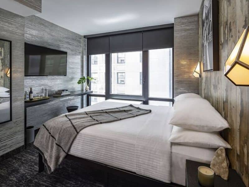 Stylish guest room at The FIDI Hotel featuring modern decor, chic lighting, plush linens, and a view of the Financial District.