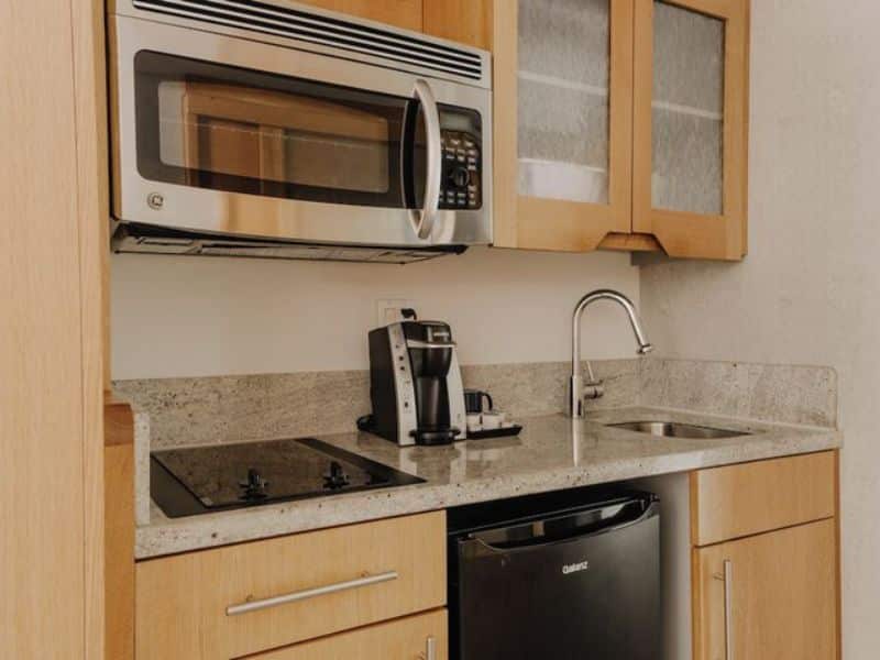 Modern kitchenette with microwave, coffee maker, stovetop, sink, and refrigerator in The Jewel Hotel, New York.